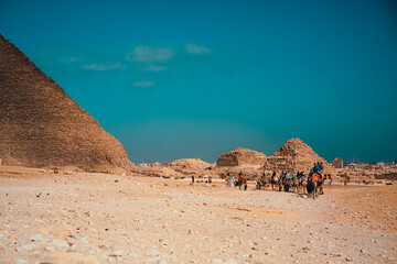 Tourists riding on camels in a convoy around the great pyramids of giza. Amazing view on a sunny...