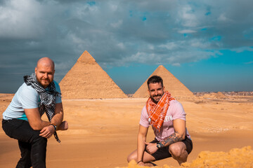 Two men travelers posing in front of the great pyramids of giza in cairo egypt. Traveling egypt during the winter, cold winter overcast day.