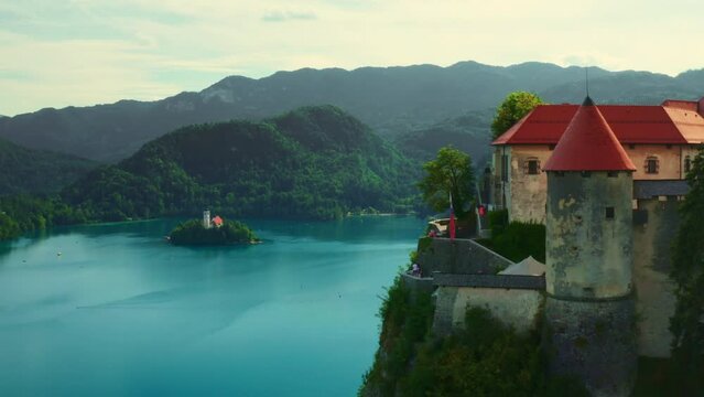 Bled castle located on high steep cliff above lake in Slovenia. Small island surrounded by blue water against giant mountains with forests. Panorama view