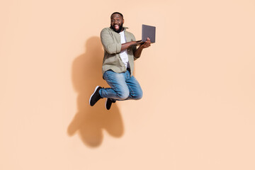 Fototapeta na wymiar Full length profile photo of cool millennial beard guy run hold laptop wear shirt jeans sneakers isolated on beige background