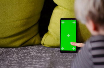 Green screen and chroma key. Caucasian woman holding mobile phone with greenscreen of chromakey mockup with tracking markers. Woman is resting at home and watching phone.