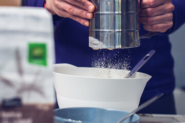 Hands straining flour for muffins preparation.