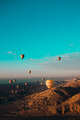 Amazing vertical shot of dozens of hot air balloons flying around the luxor egypt area. Desert orange area early in the morning. Bright blue sky - obrazy, fototapety, plakaty