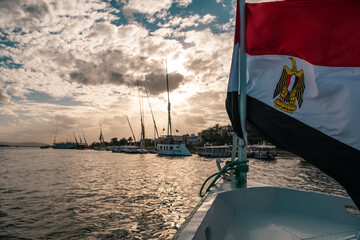 Egyptian flag waving in the wind on the front of a motor boat crusing down the river nile. Amazing view of the sunset accross the biggest river in the world