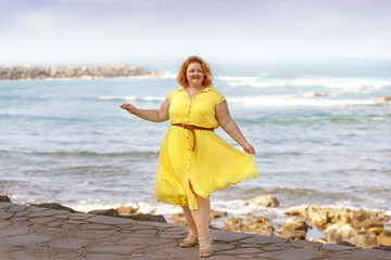 Portrait of a joyful body-positive girl in a blue dress on the background of the ocean.