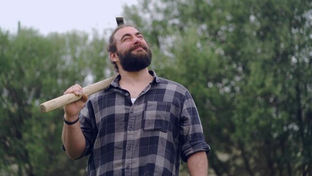 Real time of bearded male farmer with hoe looking up with dreamy face while standing in garden during harvesting season