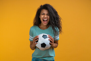 Studio image of excited soccer fan girl holding ball in hands looking at the camera with amazed face expression, celebrating her favorite team victory - 487860568