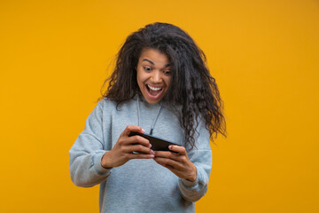 Studio portrait of happy girl reading message with good news on her mobile phone and showing...