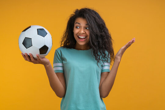 Studio portrait of beautiful happy smiling african american football supporter girl looking at the ball in her hand with surprised face expression