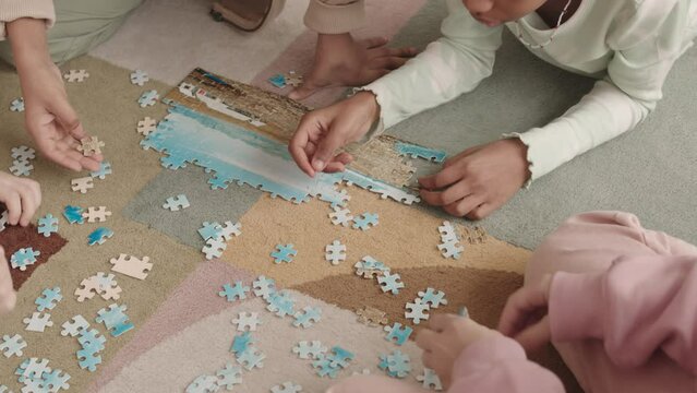 Top-view slowmo of preschool kids solving jigsaw puzzle on floor together during leisure time