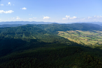 Obraz premium Aerial view of mountain hills covered with dense green lush woods on bright summer day