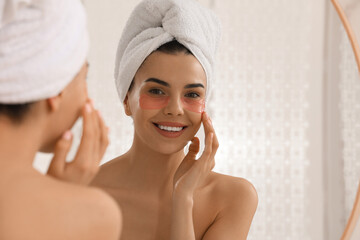 Beautiful young woman with under eye patches near mirror at home