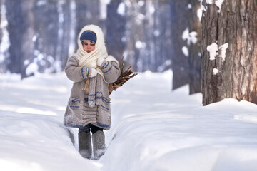 Fototapeta na wymiar Rustic winter motif. A little girl walks along a narrow snow-covered path in the forest. She is carrying a bundle of firewood. Selective focus.