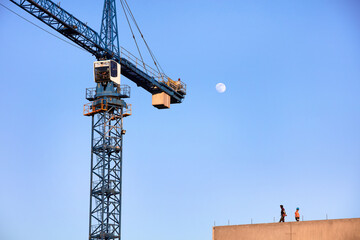 Dźwig budowlany podczas budowy domu na tle błękitnego wieczornego nieba z księżycem w pełni