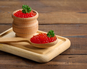 red caviar of pink salmon lies in a wooden spoon on a cutting board. Brown wooden table