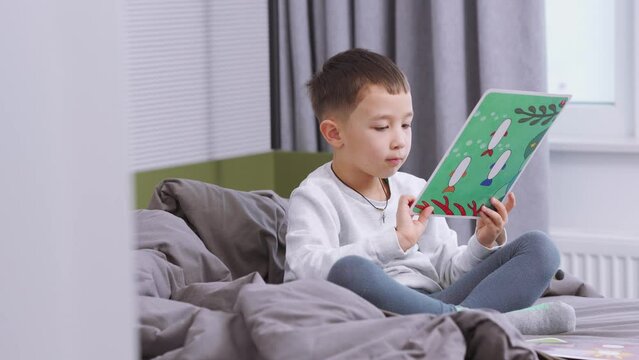 Pensive Asian little boy looking at pictures at home