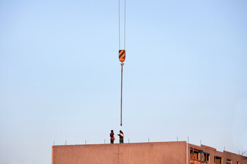 Pracownicy budowani podczas budowy domu na tle niebieskiego wieczornego nieba z dźwigiem budowlanym. - obrazy, fototapety, plakaty