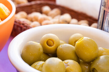 Close-up of a bowl with anchovy-stuffed olives, with dried fruit in the background. Aperitif concept.