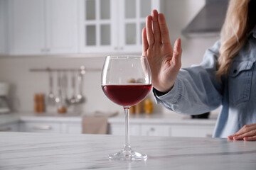 Woman refusing to drink red wine at home, closeup. Alcohol addiction treatment