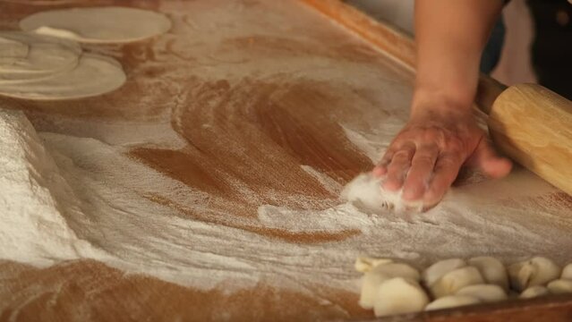 Cook sprinkling flour and rolling thin dough with roller pin at kitchen table. Woman cooking pie dough on home kitchen. Preparing Italian pizza in restaurant. Cooking handmade food concept