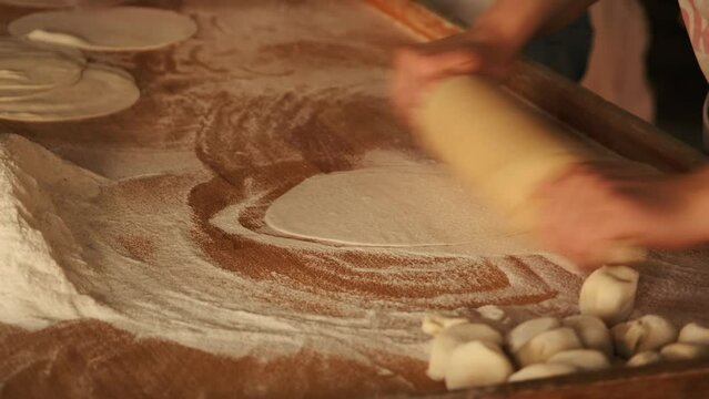 Cook sprinkling flour and rolling thin dough with roller pin at kitchen table. Woman cooking pie dough on home kitchen. Preparing Italian pizza in restaurant. Cooking handmade food concept