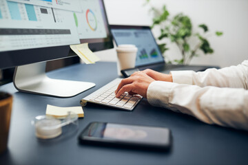 Businesswoman having video chat on mobile phone with her colleague. Businesswoman working with data on charts, graphs and diagrams on computer screen. Woman typing on keyboard sitting at desk