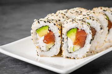 appetizing california sushi roll with cheese avocado cucumber and salmon in sesame seeds on a black...