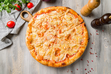 pizza Hawaiian with pineapple and chicken on grey wooden table top view