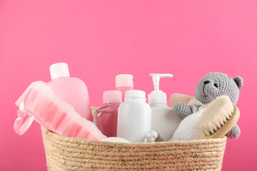 Different baby cosmetic products, bathing accessories and toy in wicker basket on pink background,...