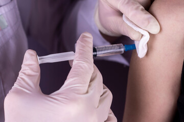 Doctor with medical gloves holding syringe with cotton disc and make injection in in the shoulder of patient. Covid-19 or coronavirus vaccine. Vaccination Close up image.