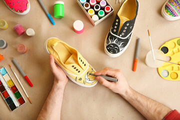 Man painting on sneaker at table, top view. Customized shoes