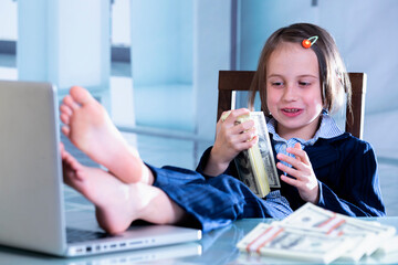 Money as the best motivator for work. Portrait of happy smiling young beautiful business girl put her feet up on a table and sniffs stacks of US Dollar bills.