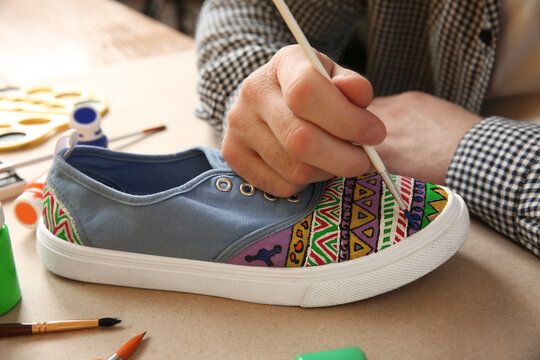 Man painting on sneaker at table, closeup. Customized shoes