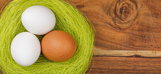 Three fresh  chicken eggs lie in a nest on wooden background with copy space. Happy Easter holiday. Top View.