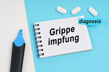 On a white and blue surface are pills, a marker and a notebook with the inscription - Grippe impfung