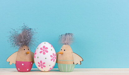 Two Easter decorative wooden chickens figurine and Easter egg on blue background with copy space. Minimal concept for Easter.
