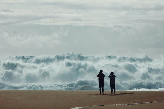 Two people taking photos of huge waves in Nazare
