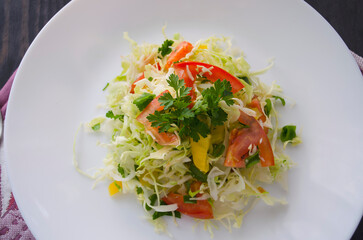 Fresh young cabbage salad on a wooden table. Peppers, tomatoes for the brightness of taste. Seasoning: sunflower oil, salt and black pepper.