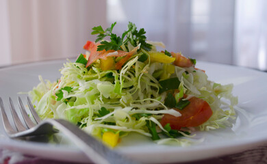 Fresh young cabbage salad on a wooden table. Peppers, tomatoes for the brightness of taste. Seasoning: sunflower oil, salt and black pepper.