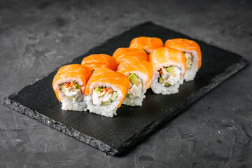 appetizing sushi roll philadelphia with avocado cheese eel cucumber and salmon on a black stone plate