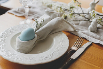Easter egg in bunny napkin on plate with cutlery, bunny, spring flowers and rustic cloth on wooden...