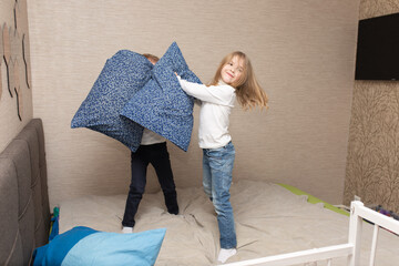Little boy and girl staged a pillow fight on the bed in the bedroom. They like that kind of game