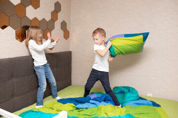 Little boy and girl staged a pillow fight on the bed in the bedroom. They like that kind of game