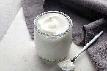 Empty white nature yogurt in glass jar on marble board with spoon and grey napkin. Simple and...