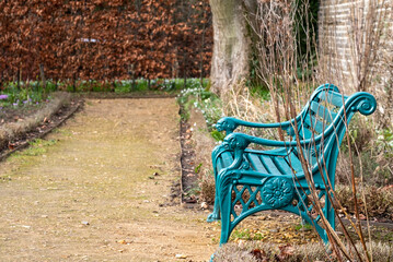 Turquoise painted ornate cast iron metal vintage retro garden bench seat, located in garden in Enfield, north London UK, with copper beech hedge in background offering contrast of colours. 
