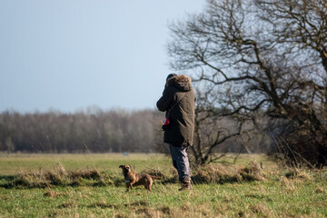 man walking his terrier cross dog across grassland field, winter blue sky