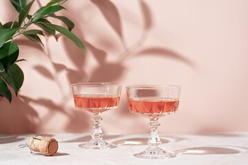 Two crystal glasses of rose sparkling wine or champagne on pastel pink marble table in sunlight....