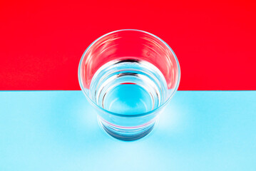 A glass with half-full water on red and blue paper, half full or half empty point of view, positive and negative mindset concept - obrazy, fototapety, plakaty