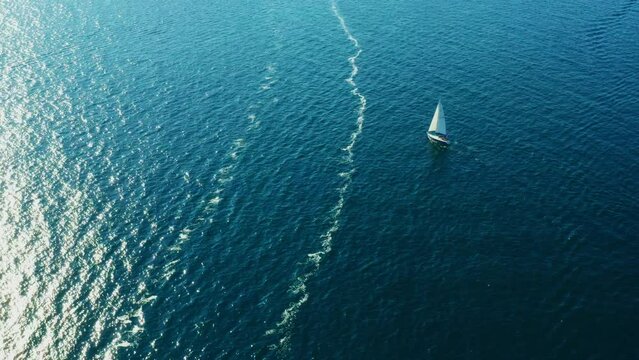 Small yacht with canvas sails in Adriatic sea on sunny day in summer. Bright sunlight reflects and flickers on dark azure water with light waves. Aerial view