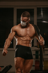 Fototapeta na wymiar A shirtless bodybuilder in a medical face mask is posing after a workout in gym